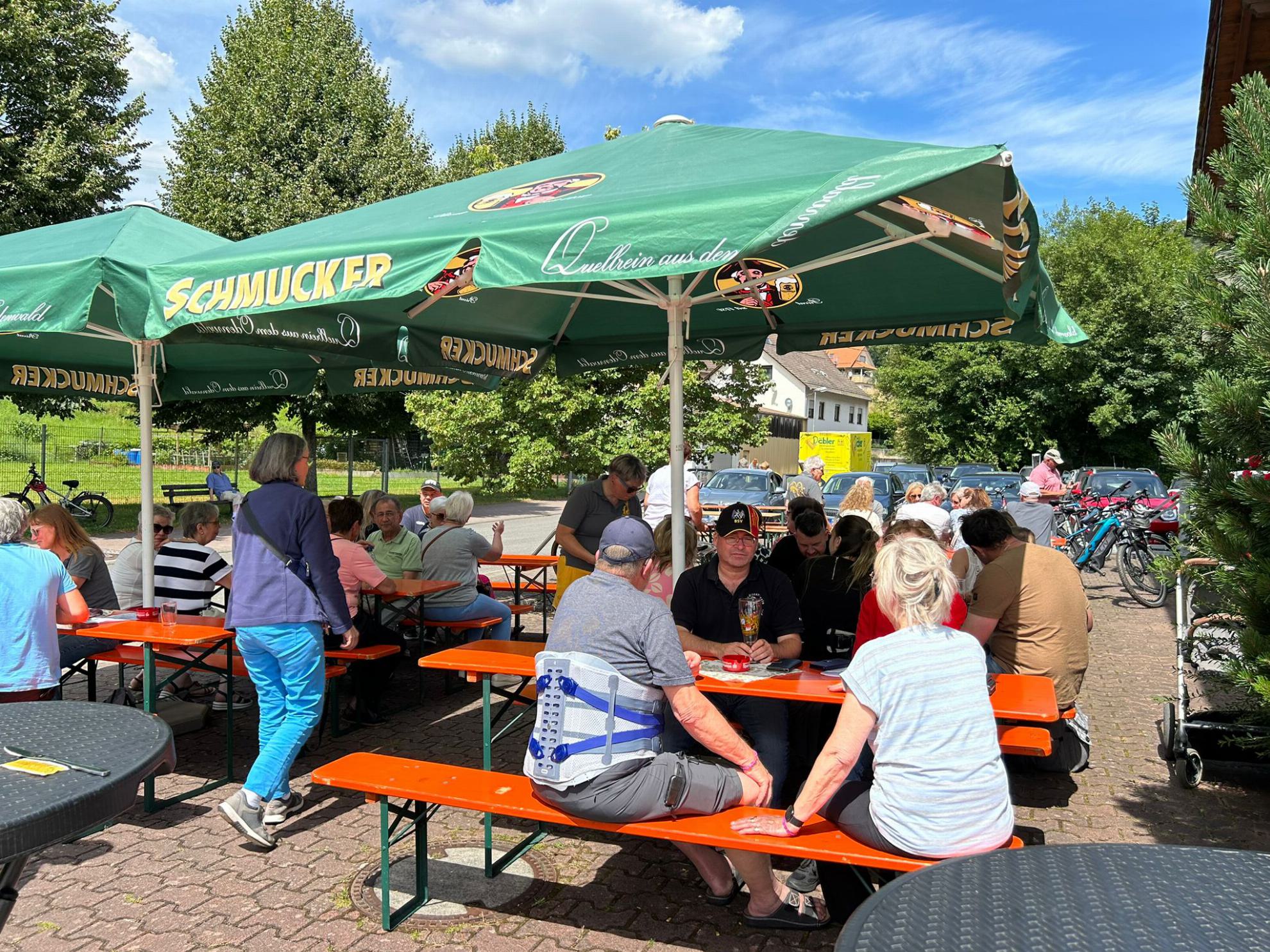 Leute sitzten auf Bierbänken unter einem grünen Sonnenschirm 